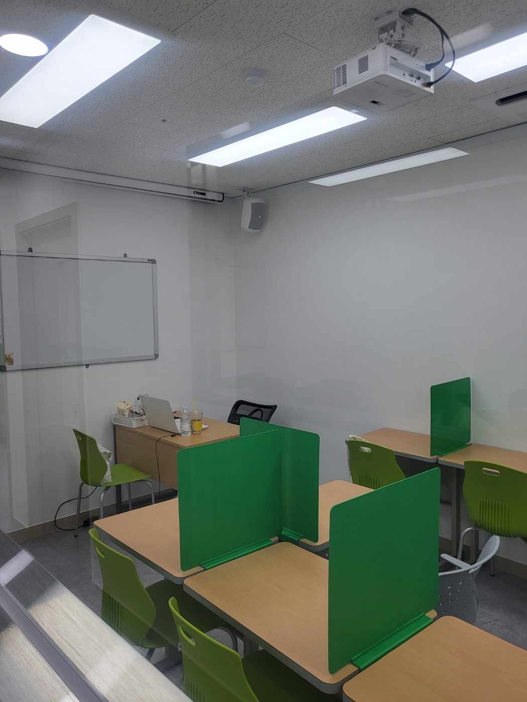 용인백현점 교실 — 천장에 빔 프로젝터가 달려 있고 왼쪽 벽에는 화이트보드가 걸려 있다. 연두색 칸막이를 세운 책상들이 놓여 있으며, 안쪽에 선생님 자리가 있다. 유리 칸막이 너머로 복도가 보인다