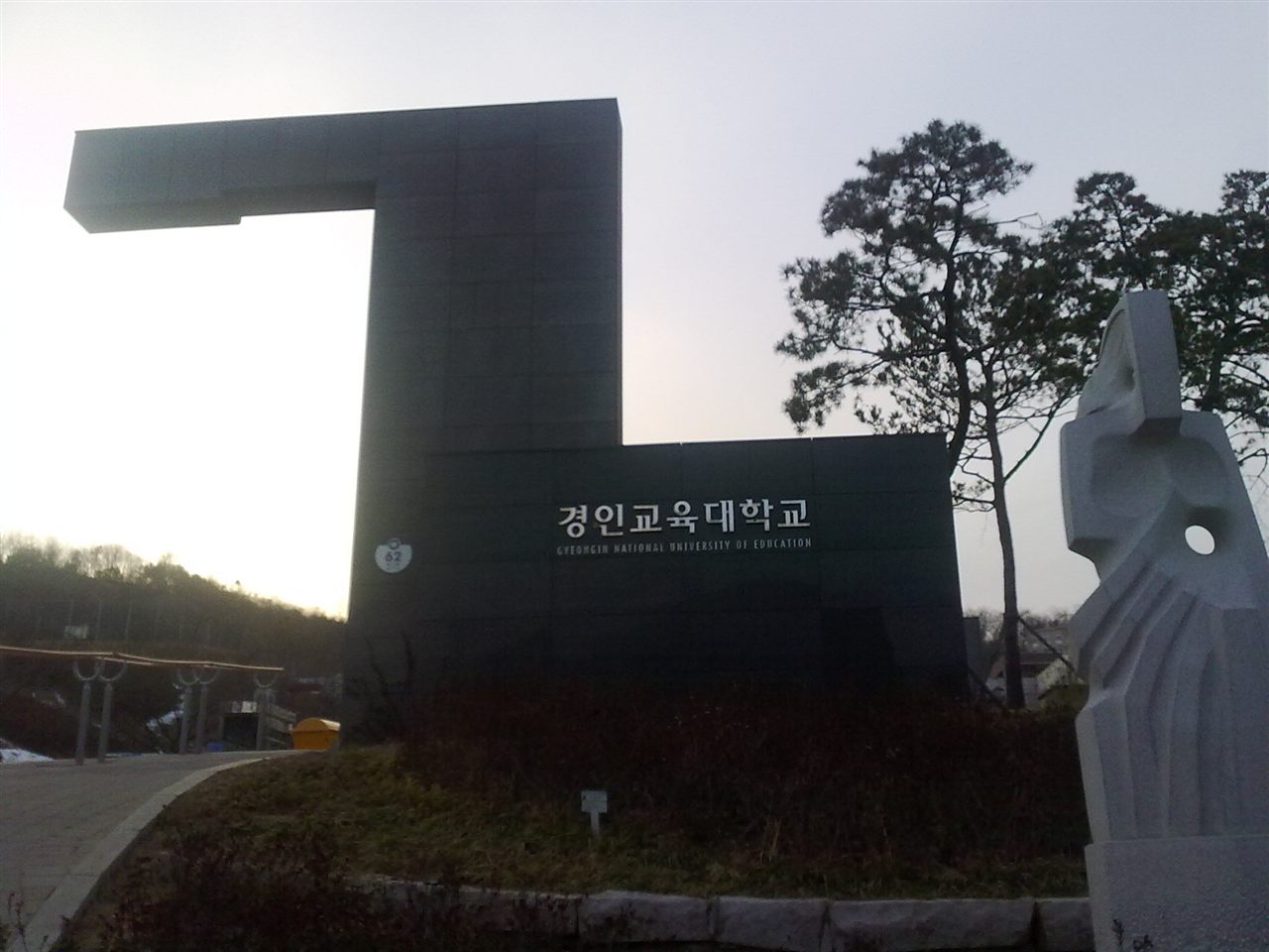 인천 계양구 경인교육대학교 인천캠퍼스 정문 — ㄱ자 모양의 검은 대형 문 구조물에 '경인교육대학교 GYEONGIN NATIONAL UNIVERSITY OF EDUCATION' 글자, 오른쪽에 흰 조각상과 소나무