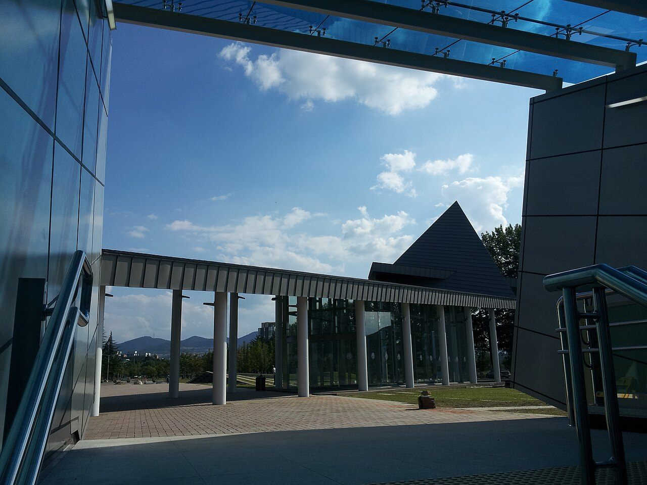 영남대학교 경산캠퍼스 정문 일대 — 흰 기둥이 늘어선 회랑과 뾰족한 삼각 지붕 건물, 멀리 보이는 산